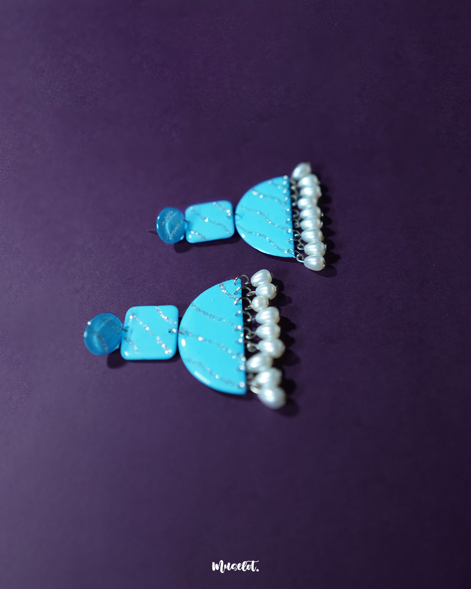 Lehrbaan blue pearl jhumkas resting against a curved neutral backdrop, highlighting the rich enamel finish and cascading pearls with a touch of elegance and depth — Muselot.