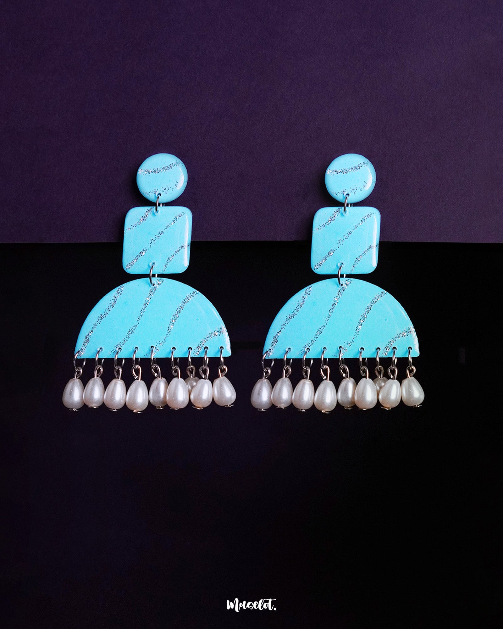 Lehrbaan drop earrings in a striking sky blue hue, detailed with silver glittery waves across geometric shapes. The semicircular base is finished with a row of dangling white pearls, creating a blend of playful charm and elegant contrast — Muselot.
