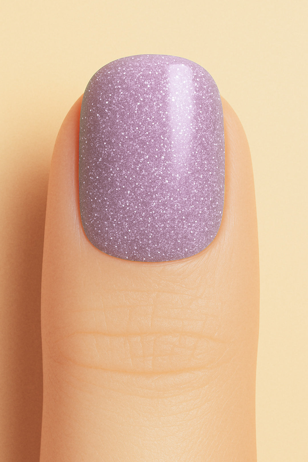 A close-up shot of a model’s finger wearing Lilac Dust Glitter nail stickies, showcasing a soft pastel lilac shade infused with fine glitter specks, creating a subtle yet elegant sparkle with a smooth, glossy finish – Muselot.