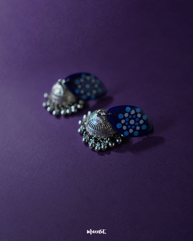 Close-up view of Meghmalhar boho jhumkas, highlighting the intricately hand-painted blue marquise tops with dotted mandala motifs in white and sky blue, paired with antique silver domes and ghungroo accents, showcasing rich detail and celebrating artisanal beauty — Muselot.