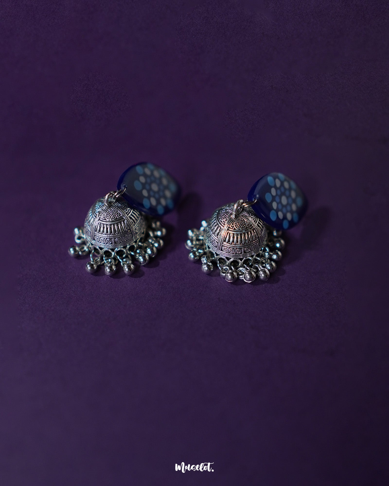 Meghmalhar boho jhumkas displayed against a soft purple backdrop, highlighting the detailed craftsmanship of the hand-painted blue tops and antique silver domes with hanging ghungroos, showcasing a fusion of tradition and artistic elegance — Muselot.