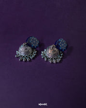 Meghmalhar boho jhumkas displayed against a soft purple backdrop, highlighting the detailed craftsmanship of the hand-painted blue tops and antique silver domes with hanging ghungroos, showcasing a fusion of tradition and artistic elegance — Muselot.