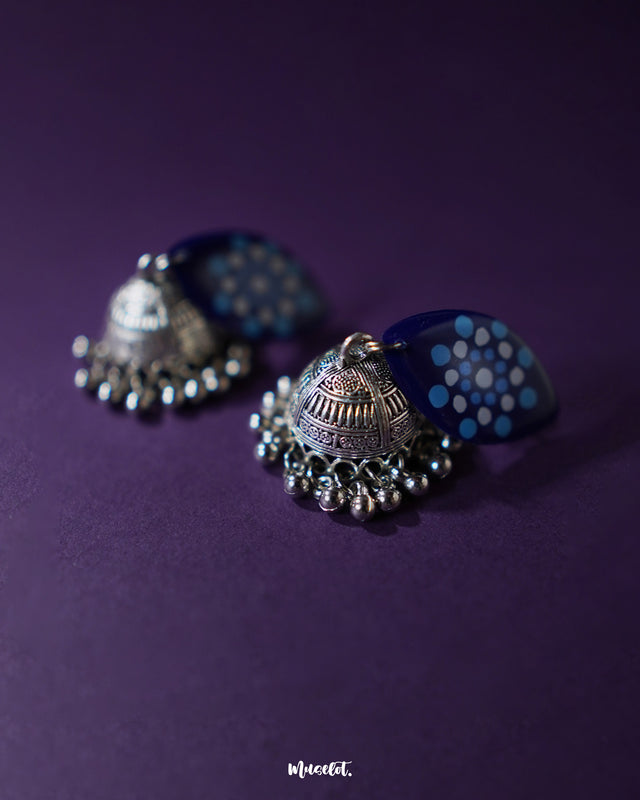 Meghmalhar boho jhumkas placed on a neutral backdrop, showcasing their vibrant blue floral tops and metallic domes with dangling ghungroos, highlighting their handcrafted finesse and traditional elegance — Muselot.
