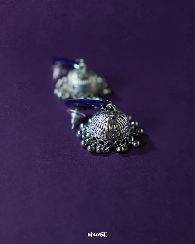 A pair of Meghmalhar boho jhumkas displayed on a flat lay, highlighting the contrast between the vivid floral studs and antique metallic dome, showcasing their artisanal charm and festive flair — Muselot.