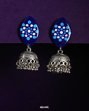 A pair of Meghmalhar jhumkas featuring deep blue marquise-shaped tops with dotted circular sky blue and white patterns, complemented by intricately detailed oxidized silver domes and ghungroo-style danglers, showcasing a striking fusion of tradition and bold design — Muselot.
