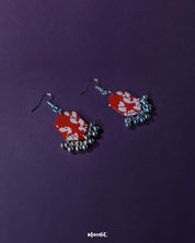 The Mehar red floral hook earrings from Muselot captured from a side angle — showcasing the dimensional depth of the hexagonal drops, the intricate white floral artwork, and the subtle sway of metallic ghungroos that lend movement and grace to the piece.