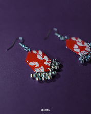 A close-up view of the Mehar red floral hook earrings from Muselot — highlighting the fine brushwork of the white floral motifs on vivid red enamel drops, with metallic ghungroos accentuating the handcrafted detail and traditional artistry.