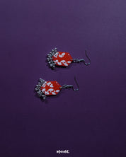 The Mehar red floral hook earrings presented in a minimal setup, highlighting the bold hexagonal shape, striking red hue, and delicate white floral detailing, with metallic ghungroos adding a subtle traditional charm to the contemporary design.
