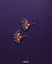 Meherbaan red floral hook earrings featuring a hand-painted tulip motif on a rich red base, adorned with delicate silver ghungroo charms, set against a deep purple backdrop — Muselot.