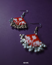 Close-up of the Meherbaan red floral hook earrings featuring hand-molded red tulip petals with intricate silver ghungroo detailing, highlighting traditional craftsmanship and showcasing festive flair — Muselot.