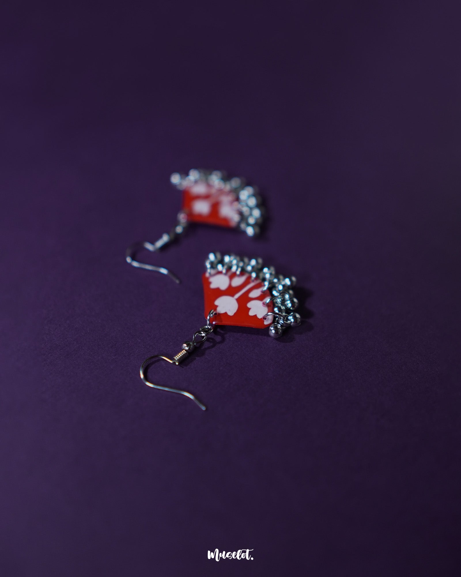 A pair of Meherbaan red floral hook earrings laid flat against a neutral backdrop, capturing the vivid red hues and delicate floral detailing that make these earrings a vibrant style statement — Muselot.