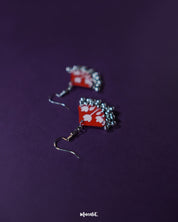 A pair of Meherbaan red floral hook earrings laid flat against a neutral backdrop, capturing the vivid red hues and delicate floral detailing that make these earrings a vibrant style statement — Muselot.
