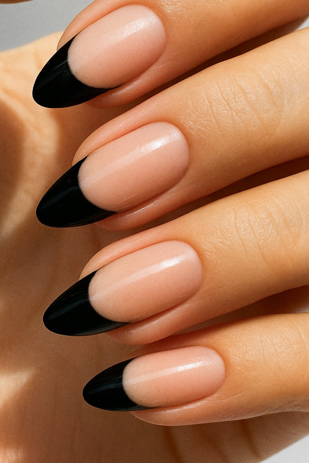 A close-up of a model’s hand wearing Midnight Tiara French Tip nail stickies, featuring a sleek black French tip design over a natural nude base. The glossy finish highlights the sharp contrast, giving a bold yet elegant twist to the classic French manicure style – Muselot.