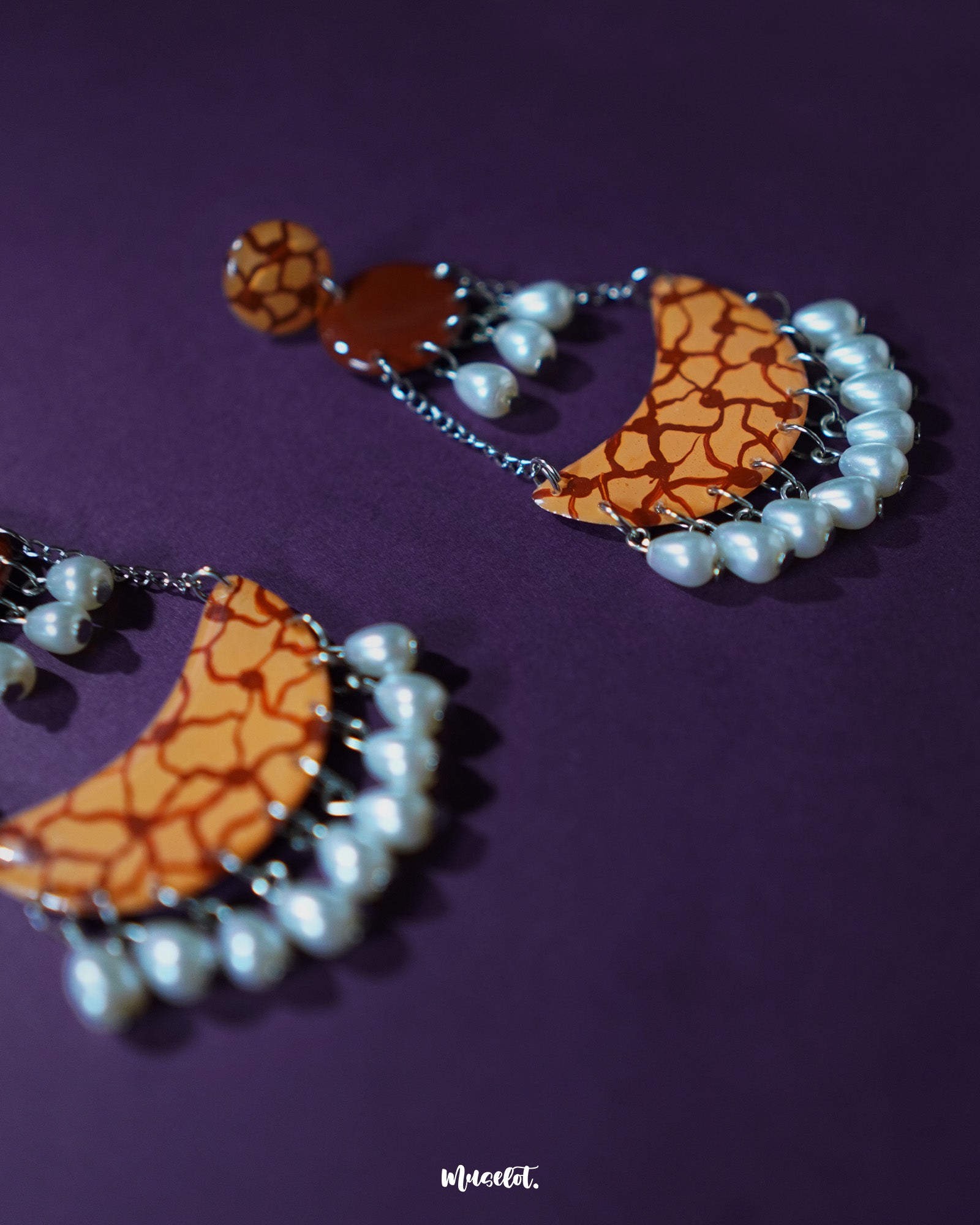 The Mittika chandbali earrings lie gracefully on a neutral backdrop, highlighting their crescent-shaped frame adorned with intricate motifs and white pearl accents that exude ethnic charm and festive elegance — Muselot.