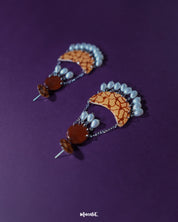 Mittika chandbali earrings displayed against a deep purple background, showcasing their bold orange crackle pattern and delicate pearl danglers for a vibrant, handcrafted charm — Muselot.