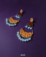 The Mittika chandbali earrings rest on a textured brown surface, highlighting the intricate floral enamel work, clustered pearls, and oxidized silver detailing that together create a vintage yet vibrant appeal — Muselot.