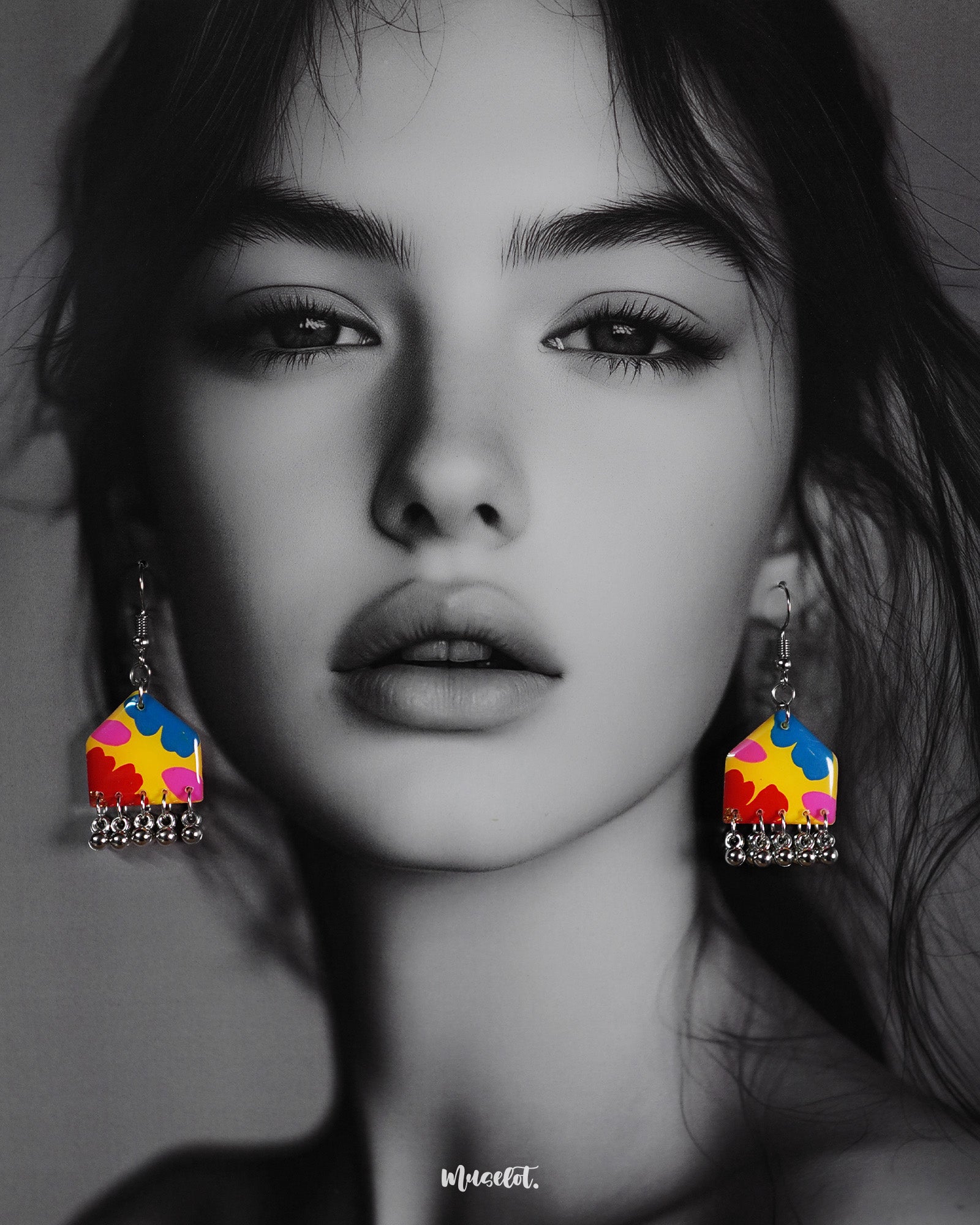 A model wears the multicolor floral earrings, showcasing their vibrant palette of red, blue, yellow, and pink florals with dangling silver ghungroos, adding a playful and colorful charm to the overall look — Muselot.