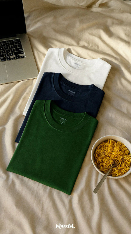 Combo of unisex cotton T-shirts in olive green, navy blue, and classic white, laid out on a soft, textured beige background, showcasing their smooth finish, relaxed fit, and everyday-wear appeal. The calm earthy and neutral tones of the background amplify the cozy, chill vibe perfect for Netflix and unwinding — Muselot.