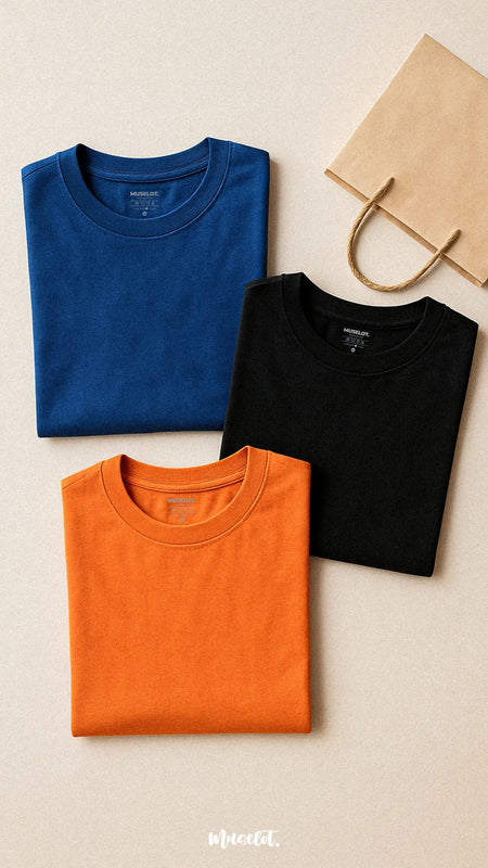 Three cotton T-shirts in royal blue, jet black, and rust orange, neatly laid out side by side on a smooth neutral surface, showcasing their vibrant colors and soft texture, perfect for everyday style on a budget — Muselot.