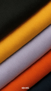 A close-up shot of soft cotton knit fabric in vibrant shades of black, mustard, lavender, orange, and navy, showcasing the fine weave, smooth texture, and premium quality — Muselot