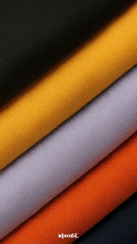 A close-up shot of soft cotton knit fabric in vibrant shades of black, mustard, lavender, orange, and navy, showcasing the fine weave, smooth texture, and premium quality — Muselot