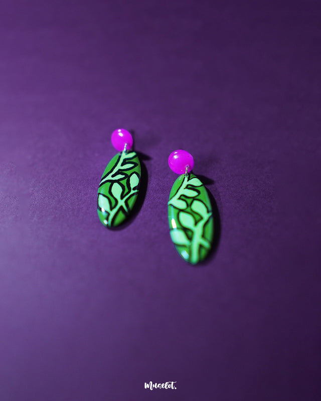 A zoomed-in shot of the Naghma green leaf drop earrings placed against a soft background, showcasing the detailed leaf design, glossy green finish, and the elegant pink stud top — Muselot.