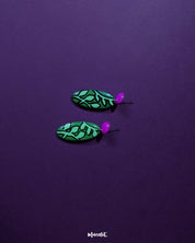 A detailed view of the Naghma green leaf drop earrings laid out flat, highlighting the bold green enamel, delicate black veining, and pink stud tops that bring a refreshing, nature-inspired charm — Muselot.