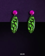 A pair of Naghma leaf drop earrings featuring a vivid green leaf motif on elongated oval shapes, topped with glossy magenta studs, highlighting the bold contrast and showcasing their artistic, nature-inspired design — Muselot.