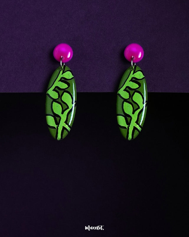 A pair of Naghma leaf drop earrings featuring a vivid green leaf motif on elongated oval shapes, topped with glossy magenta studs, highlighting the bold contrast and showcasing their artistic, nature-inspired design — Muselot.
