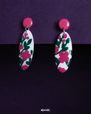 Nargis floral drop earrings displayed against a dual-tone purple background, highlighting the hand-painted pink and green floral patterns on white ovals, showcasing the charm of handmade artistry — Muselot.
