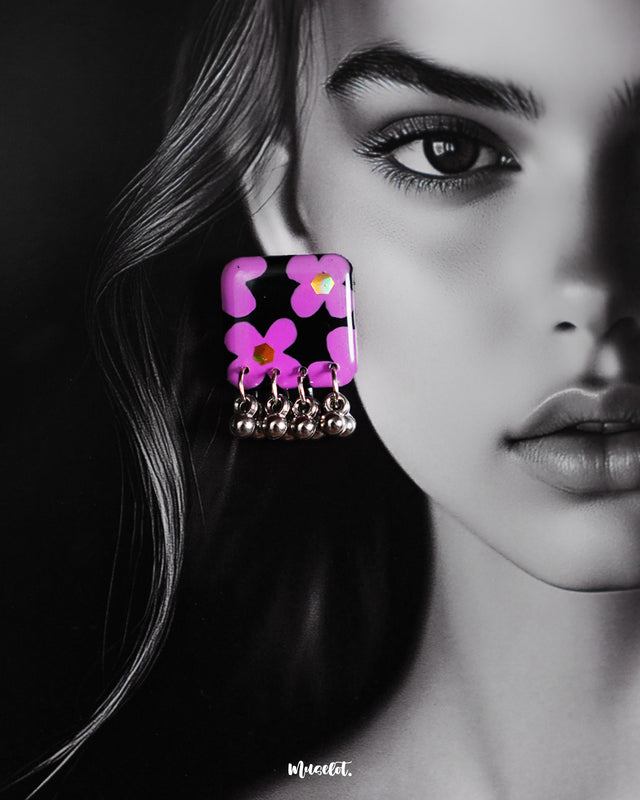 A model gracefully presents the Naubahar handmade earrings, featuring vibrant lavender flowers delicately crafted to create a harmonious blend of elegance and charm. The earrings, set against a soft purple background, offer a refined look perfect for enhancing any outfit with a touch of floral sophistication — Muselot