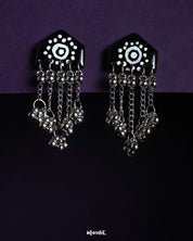 Nazafar black handcrafted earrings with painted white circular motifs and cascading silver ghungroo chains, displayed on a dark background – Muselot.