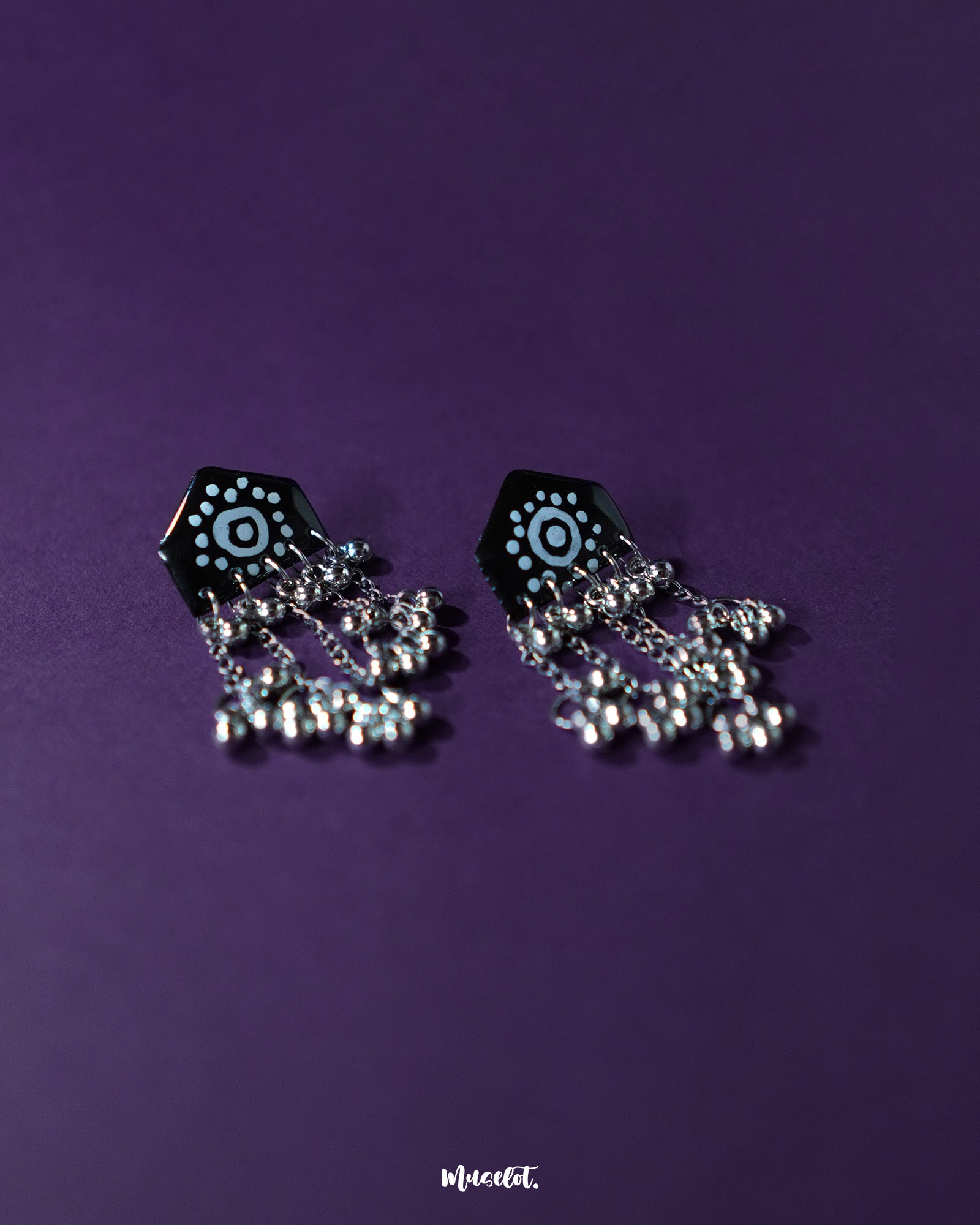 Pair of Nazafar black jhumkas laid flat on a neutral background, showcasing bold white painted motifs while highlighting the oxidized silver dome and ethnic artistry – Muselot.