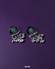 Pair of Nazafar black jhumkas laid flat on a neutral background, showcasing bold white painted motifs while highlighting the oxidized silver dome and ethnic artistry – Muselot.
