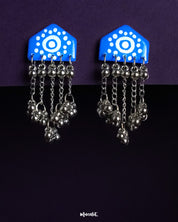 Nazafar blue handcrafted earrings with white circular motifs and cascading silver ghungroo chains, displayed against a purple background – Muselot.