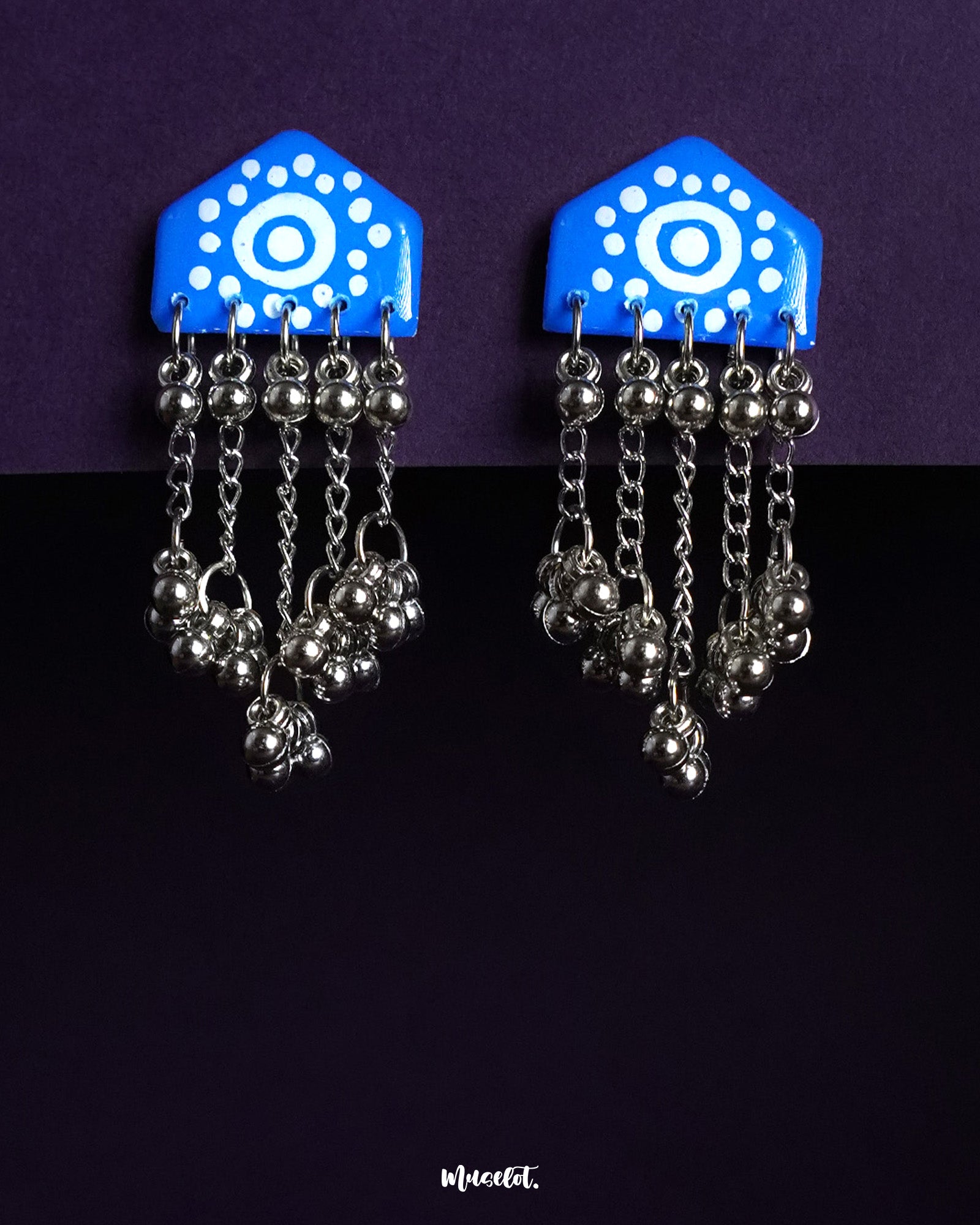 Nazafar blue handcrafted earrings with white circular motifs and cascading silver ghungroo chains, displayed against a purple background – Muselot.