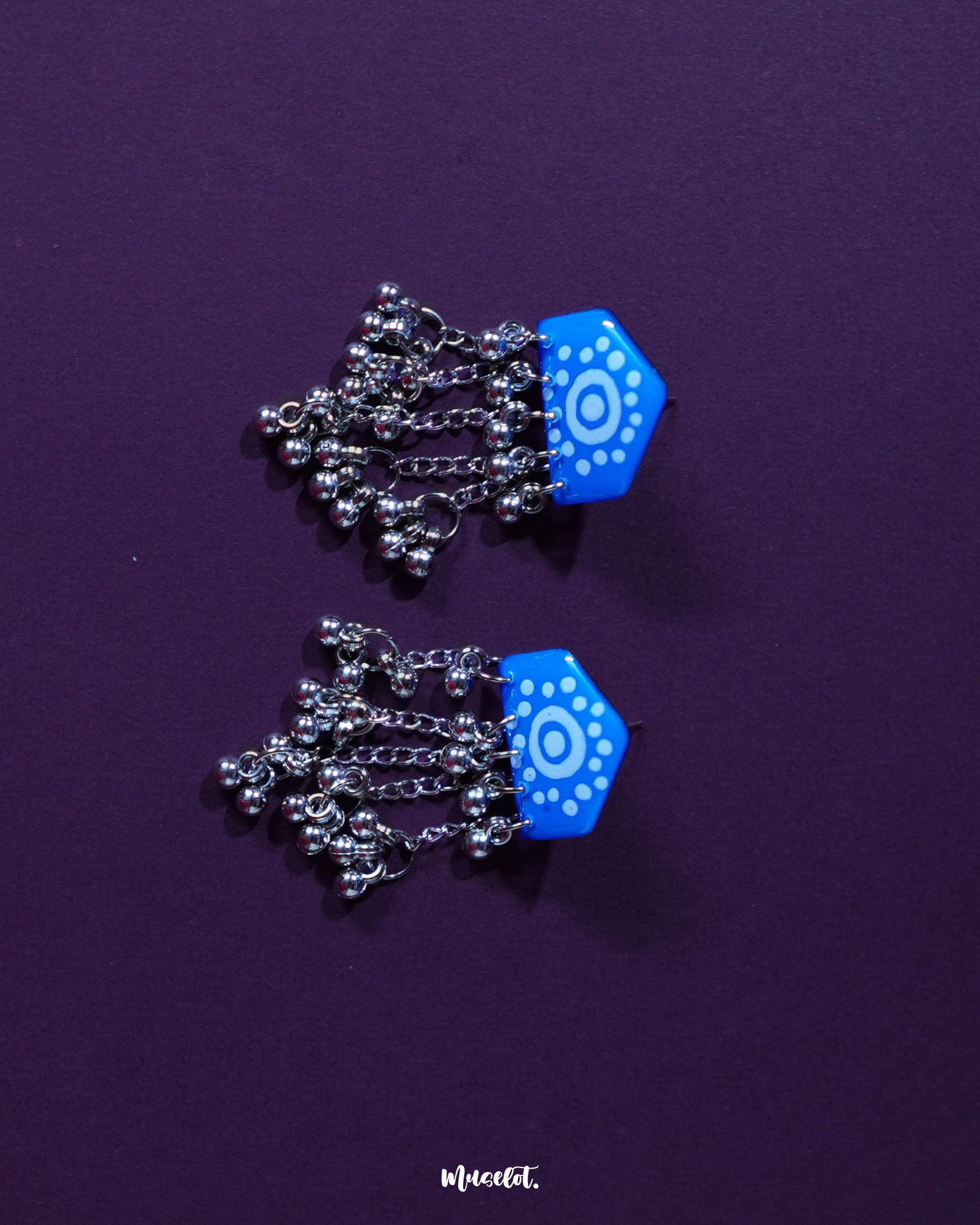 Nazafar blue handcrafted jhumkas angled against a plain backdrop, showcasing the bold white circular motifs while highlighting the antique silver dome and traditional elegance – Muselot.
