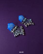 Nazafar blue jhumkas captured in a close view, showcasing intricate white motif detailing while highlighting the oxidized silver dome and ethnic artistry – Muselot.