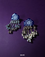 Nazafar dark blue jhumkas displayed on a plain backdrop, showcasing bold white motif accents while highlighting the oxidized silver dome and traditional handcrafted charm – Muselot.