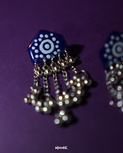 Pair of Nazafar dark blue jhumkas laid flat on a neutral surface, showcasing hand-painted white motif work while highlighting the oxidized silver dome and cultural craftsmanship – Muselot.