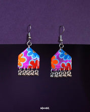 Nazrana hand-painted hook earrings with multicolour floral motifs on a purple-red base and silver ghungroo drops, displayed against a deep purple background – Muselot.