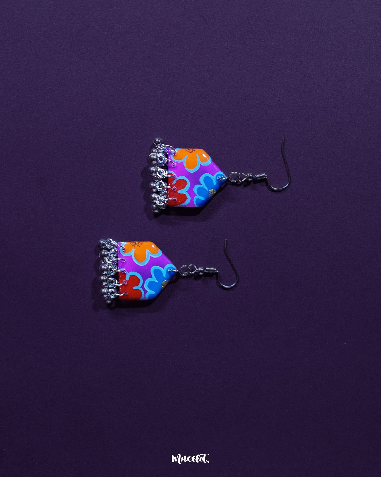 Pair of Nazrana multicolour floral earrings laid flat, featuring hand-painted motifs and dangling silver ghungroo details on a neutral backdrop – Muselot.