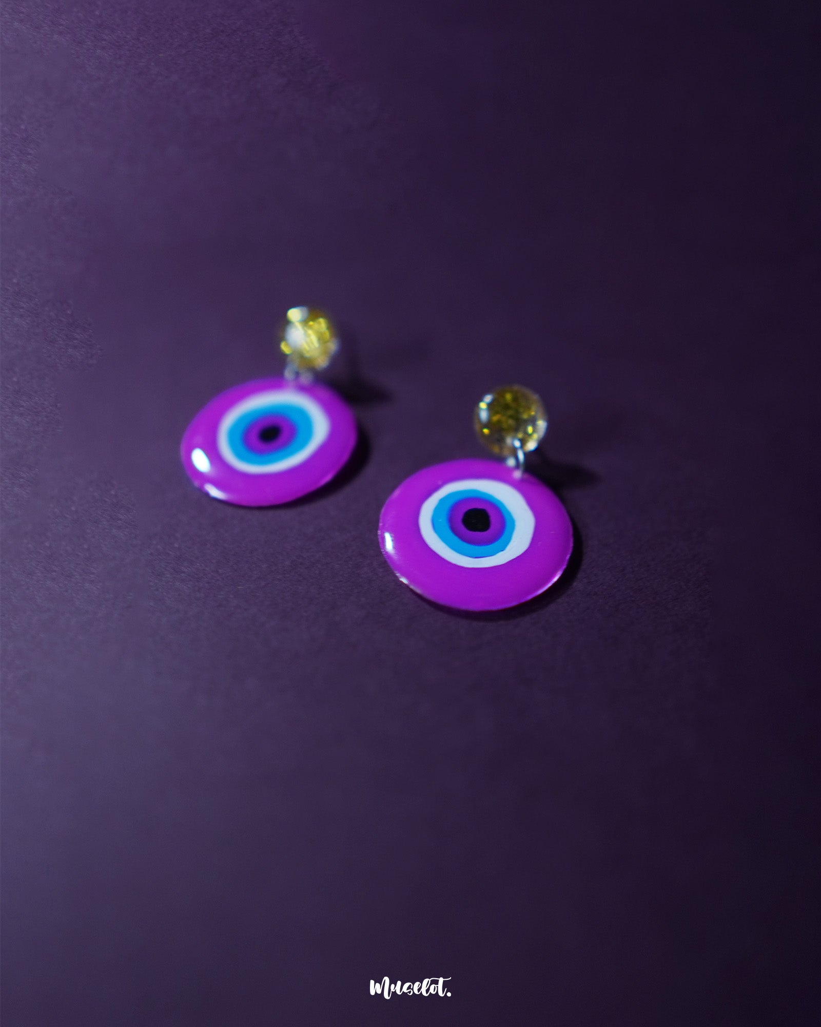 A close-up of the Nigaahbaan evil eye stud earrings reveals their glossy magenta finish and bold concentric design—anchored by golden glitter studs