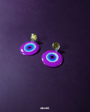 A close-up of the Nigaahbaan evil eye stud earrings reveals their glossy magenta finish and bold concentric design—anchored by golden glitter studs