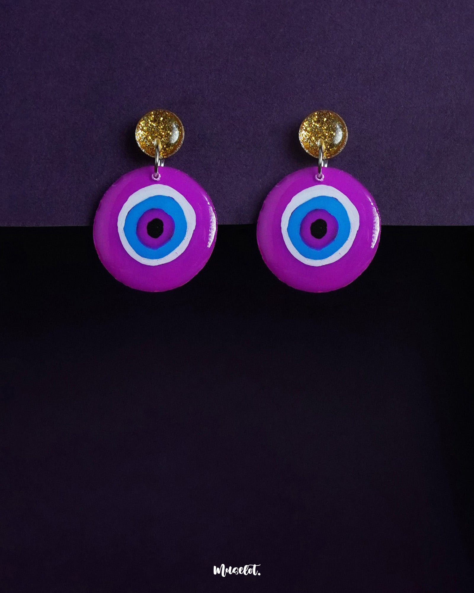 A bold and playful pair of Nigaahbaan stud earrings, featuring a hand-painted evil eye motif in vivid purples and blues, anchored by shimmering golden studs—perfect for warding off the ordinary — Muselot.
