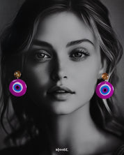 A model flaunting the Nigaahbaan stud earrings, where the golden glitter tops meet bold concentric circles of blue, white, and black on a vivid magenta base—an eye-catching fusion of charm and tradition — Muselot.