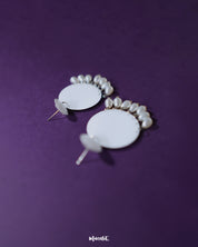 A pair of Noor white drop earrings photographed from a side angle, revealing their sleek glossy finish and delicate pearl danglings that enhance the soft, elegant appeal — Muselot.
