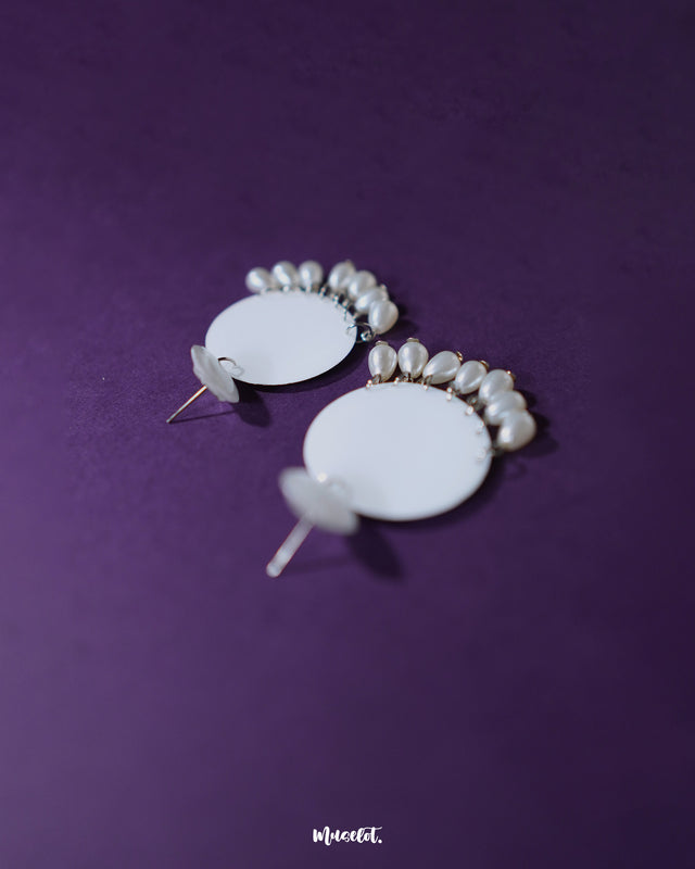 A pair of Noor white drop earrings photographed from a side angle, revealing their sleek glossy finish and delicate pearl danglings that enhance the soft, elegant appeal — Muselot.