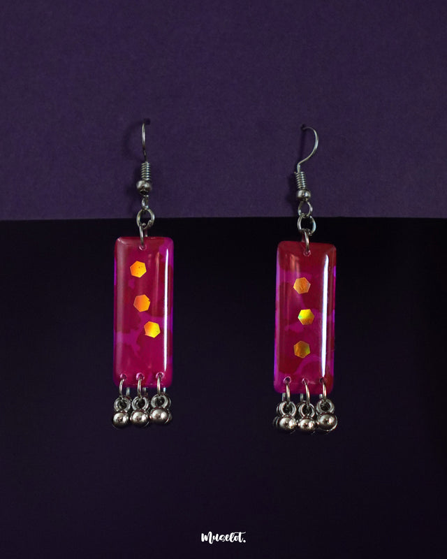 Noorasa pink drop earrings placed against a purple-toned backdrop, highlighting their dainty floral design and soft feminine elegance – Muselot