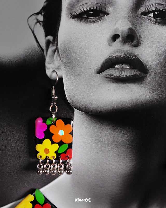 A zoomed-in shot of the model wearing the Parizad floral earrings from the set, showcasing the vivid hand-painted flowers in yellow, pink, orange, and red over a black base. The silver gungroo drops add a playful touch, making the earrings a standout boho statement — Muselot.